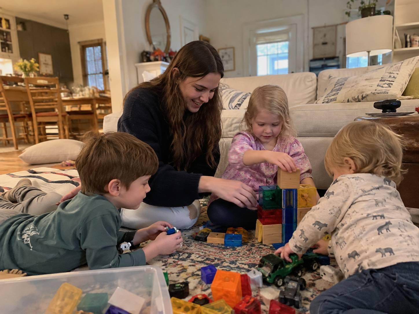 An au pair playing with 2 little children in the living room